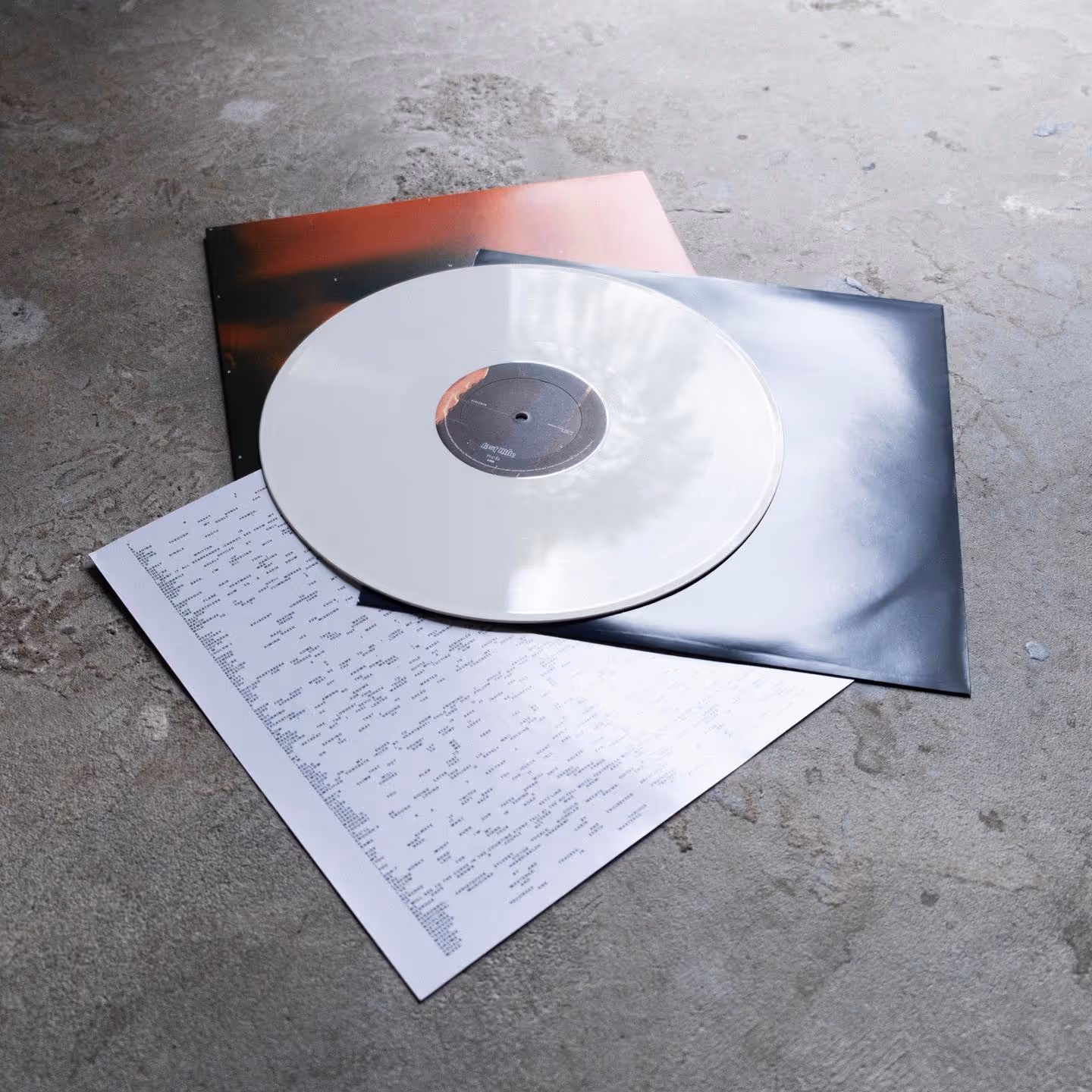 White vinyl record partially placed on two album covers and a printed lyric sheet on a concrete surface.