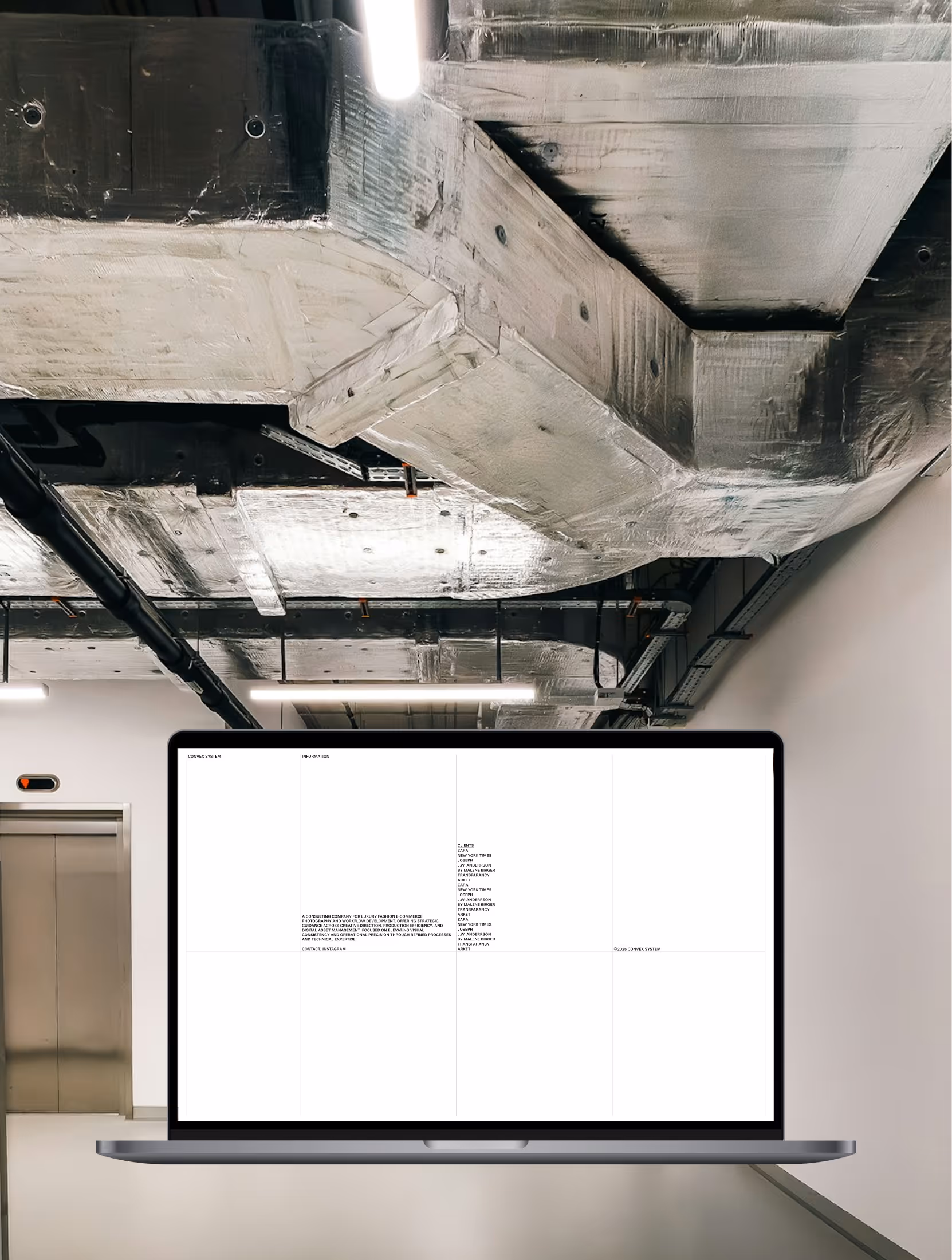 Laptop displaying a webpage with black text on white background, set against an industrial ceiling and elevator backdrop.