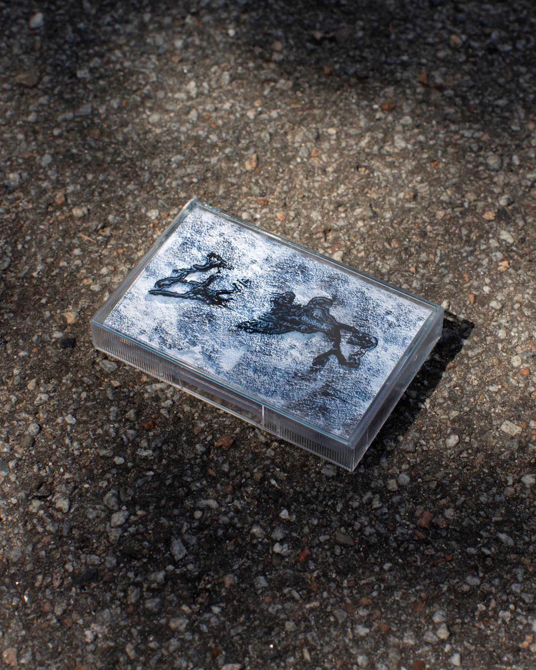 Rectangular clear plastic case with artistic black ink drawings on a white textured background inside, placed on rough gravel ground.